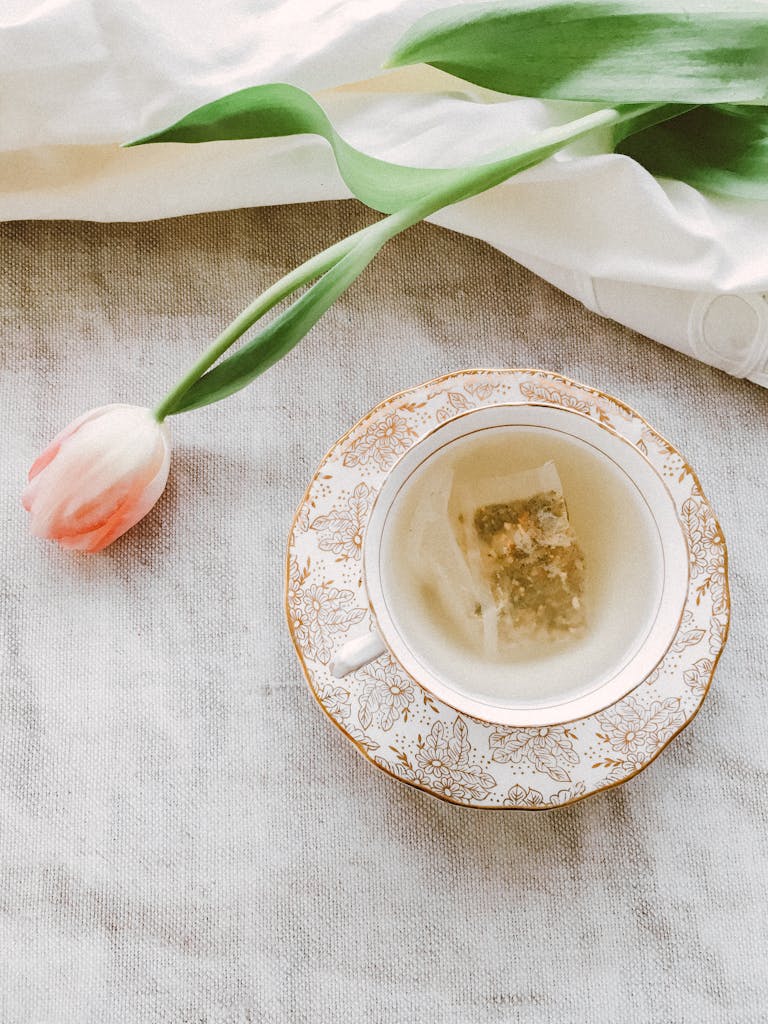 A delicate tea scene with herbal tea in a floral porcelain cup beside a pink tulip.